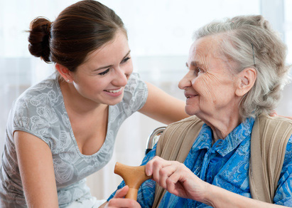 Seniorin sitzt zufrieden in ihrem Wohnzimmer in Münster, Betreuungskraft unterstützt bei Alltagsaufgaben. Professionelle Seniorenbetreuung und Pflege zuhause.
